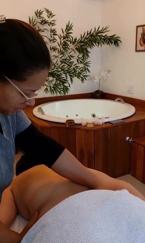 Massagem na sala de spa, com o ofurô de madeira ao fundo
